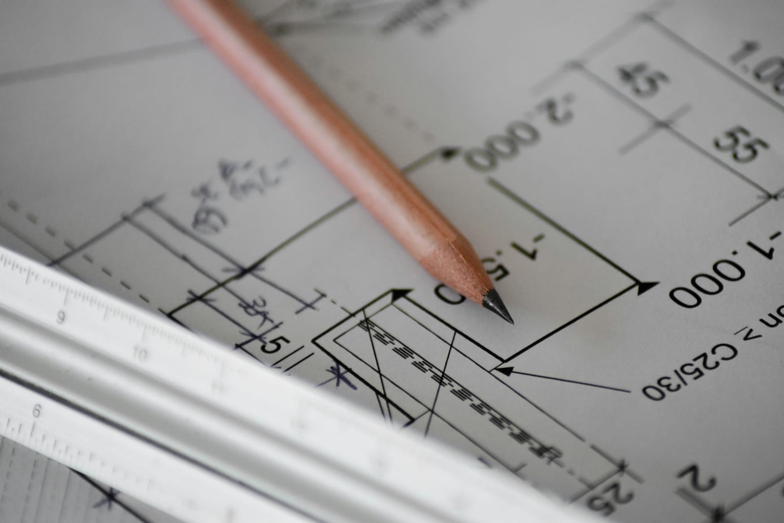 Close-up of a printed structural drawing with dimensions and level marks, a sharpened pencil and a triangular scale rule.