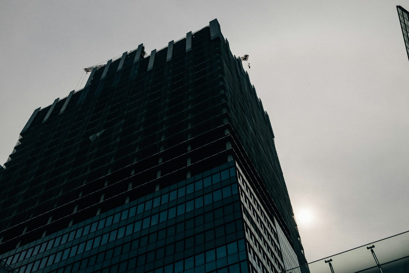 Low-angle view of a tower under construction in grey light, glazed curtain wall finished on the lower floors and the upper floors still open.